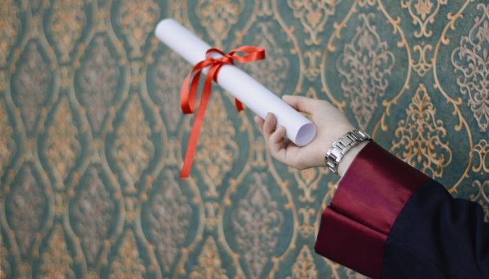 A graduate's hand holding a diploma with red ribbon, symbolizing achievement.